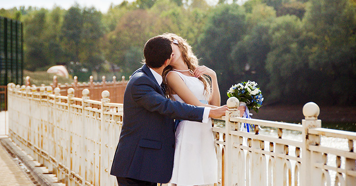 bride and groom kissing on a bridge