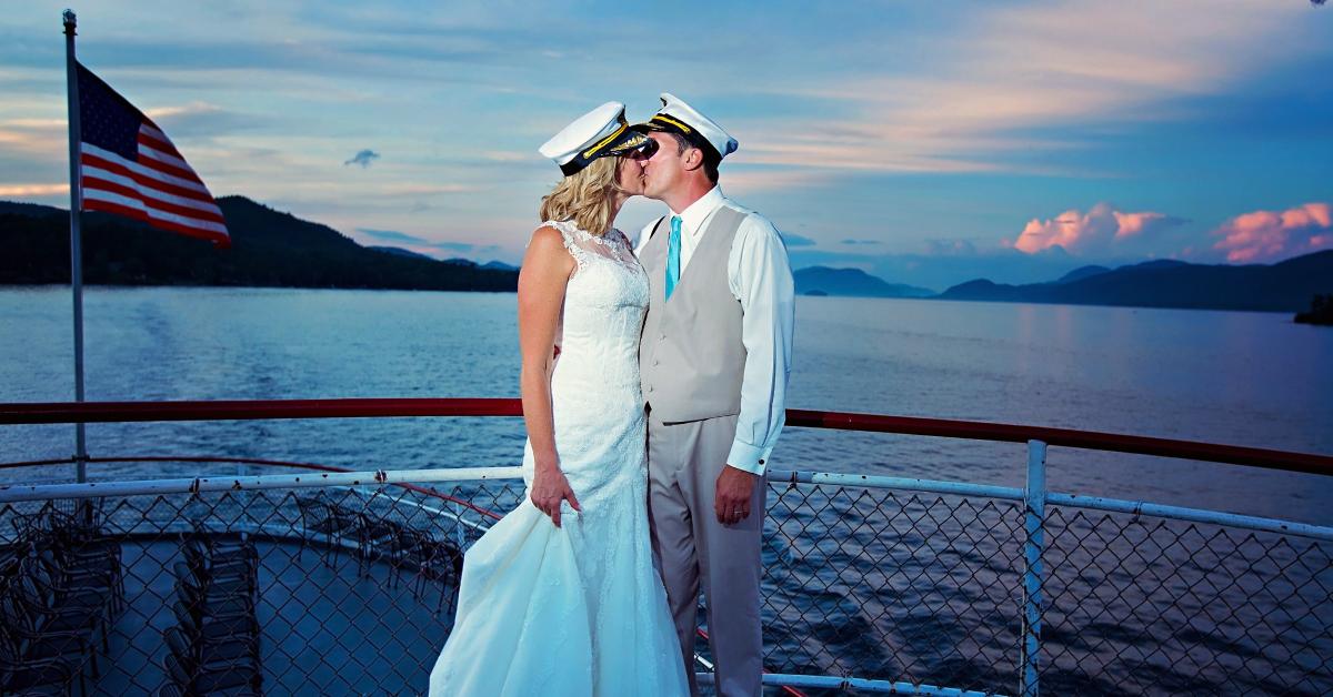 bride and groom kissing on a boat with the mountains in the background