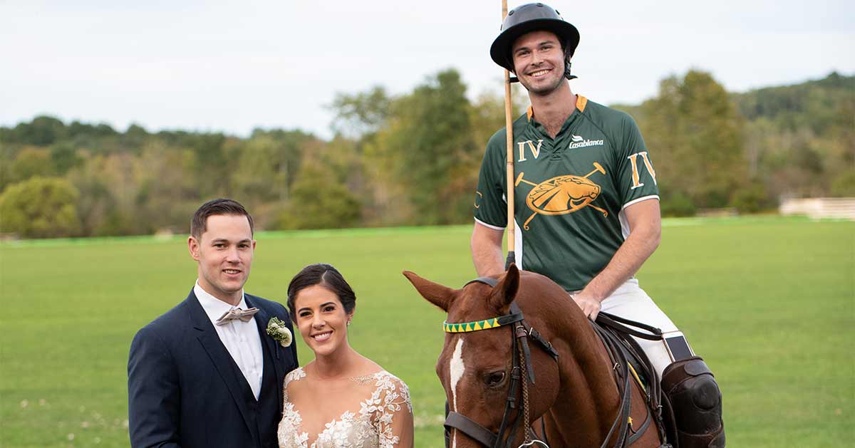 A bride and groom pose with a polo player.